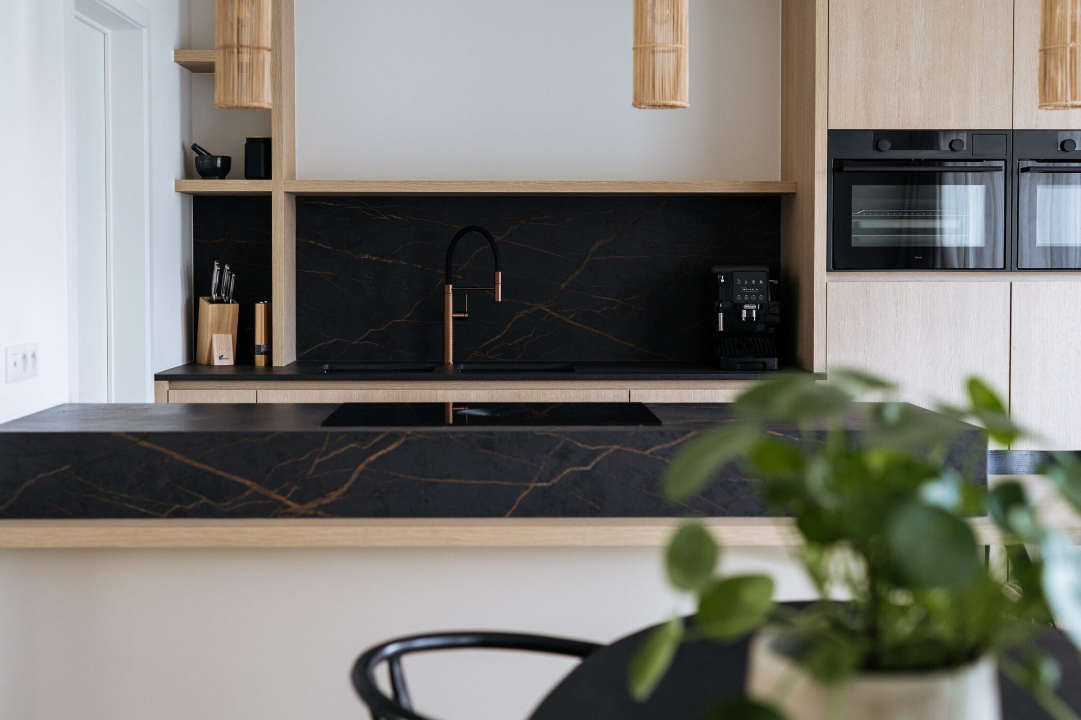 Moderne keuken met zwarte spatwand, koperen kraan en lichte houten fronten achter het eiland in Knokke-Heist, Kaster Keukens