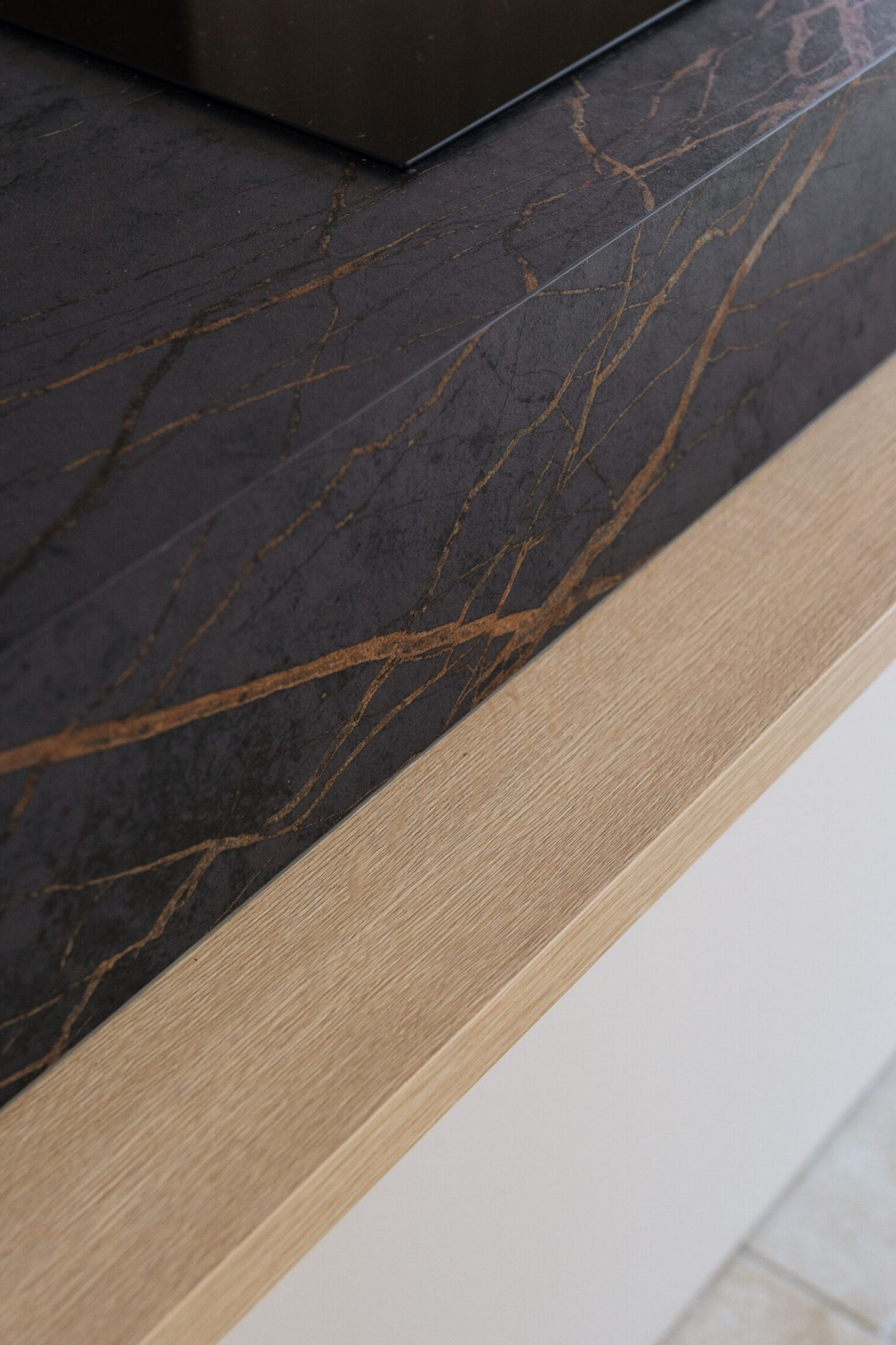 Detail van een moderne keuken met zwart werkblad met gouden aders op een lichte houten rand in Knokke-Heist, Kaster Keukens