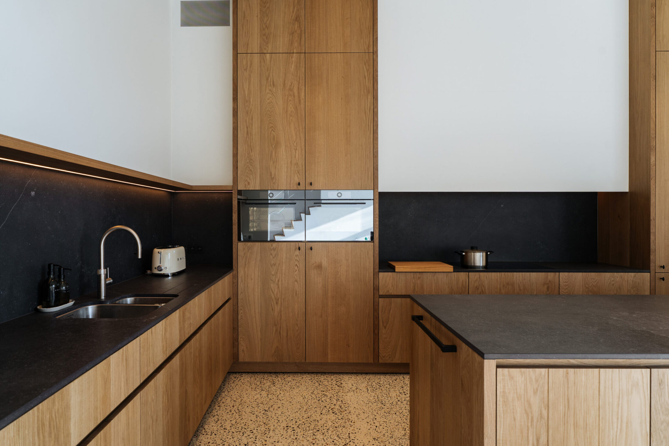 Moderne keuken met eiken fronten, donker werkblad en zwarte spatwand in Kortrijk, Kaster Keukens