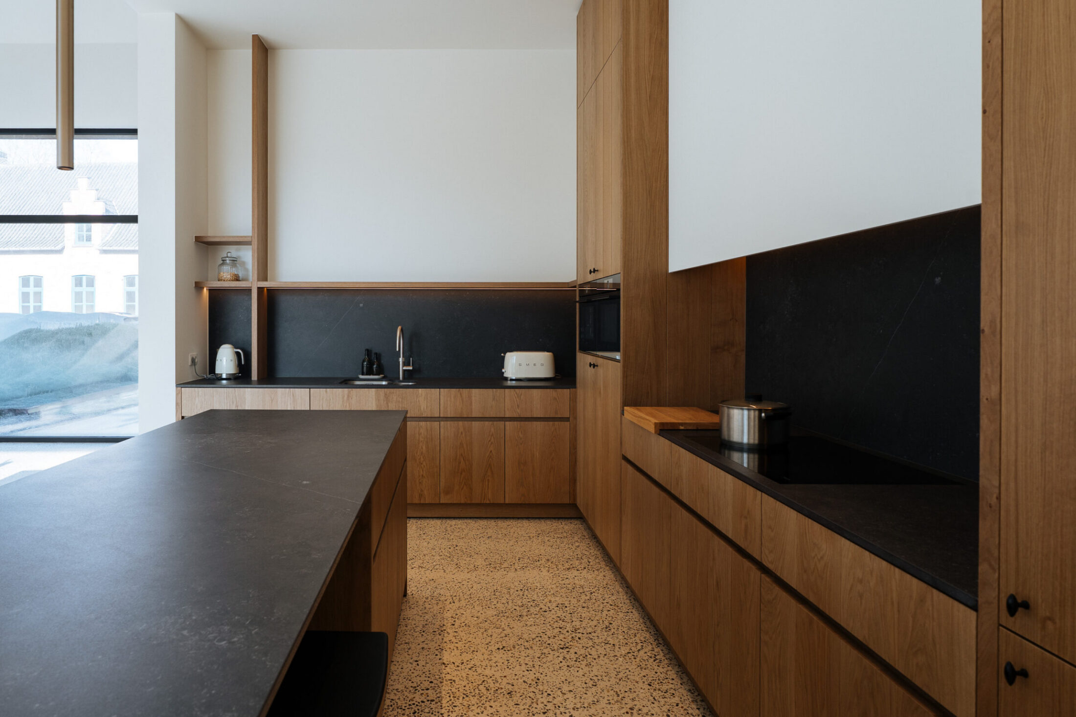 Moderne keuken met eiken kastenwand, donker kookeiland en zwarte spatwand in Kortrijk, Kaster Keukens