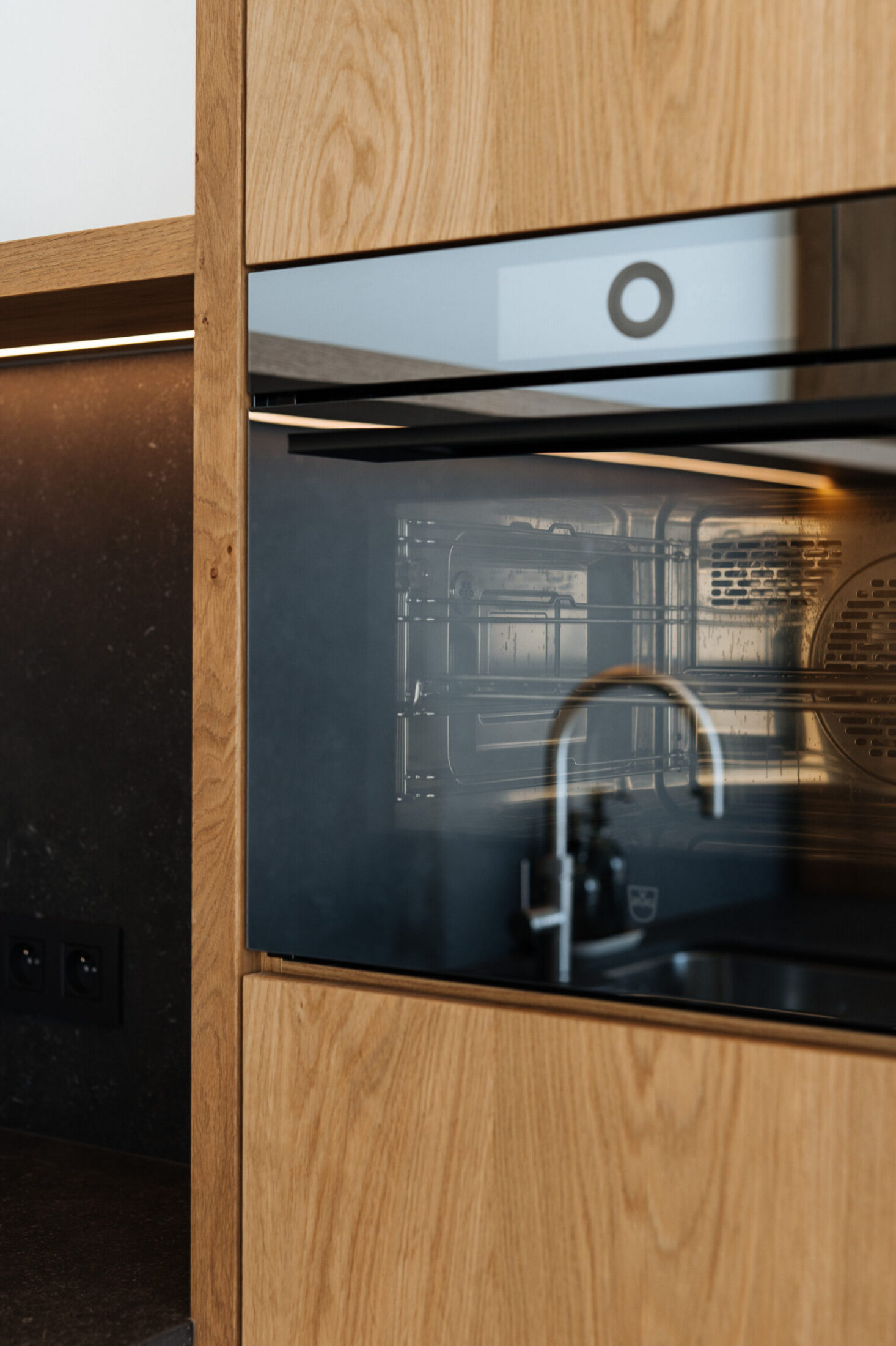 Detail van een moderne keuken met eiken fronten, zwarte inbouwoven en zwarte kraan in Kortrijk, Kaster Keukens
