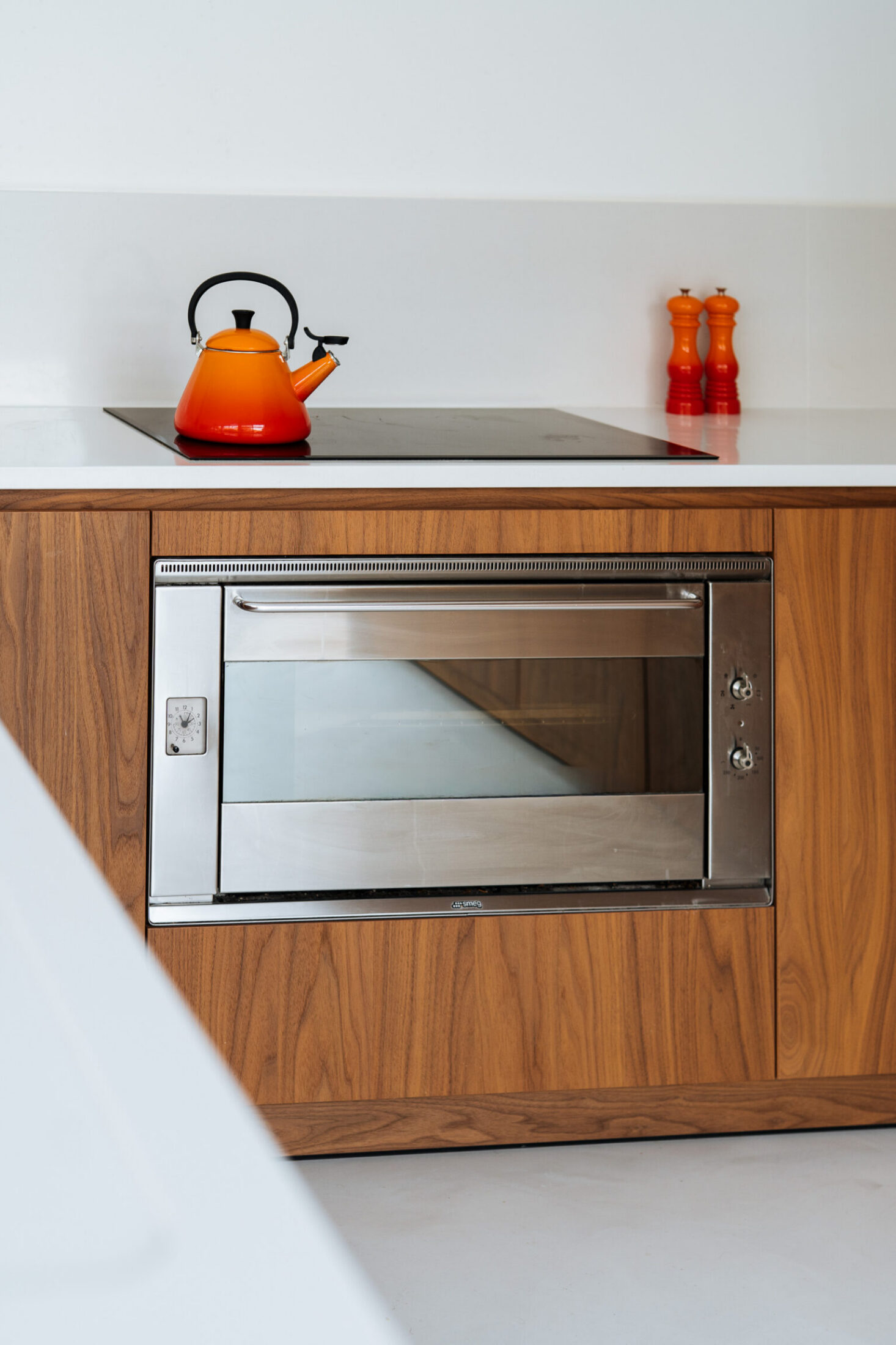 Detail van een moderne keuken met houten fronten, inox oven en oranje waterkoker in Kortrijk, Kaster Keukens