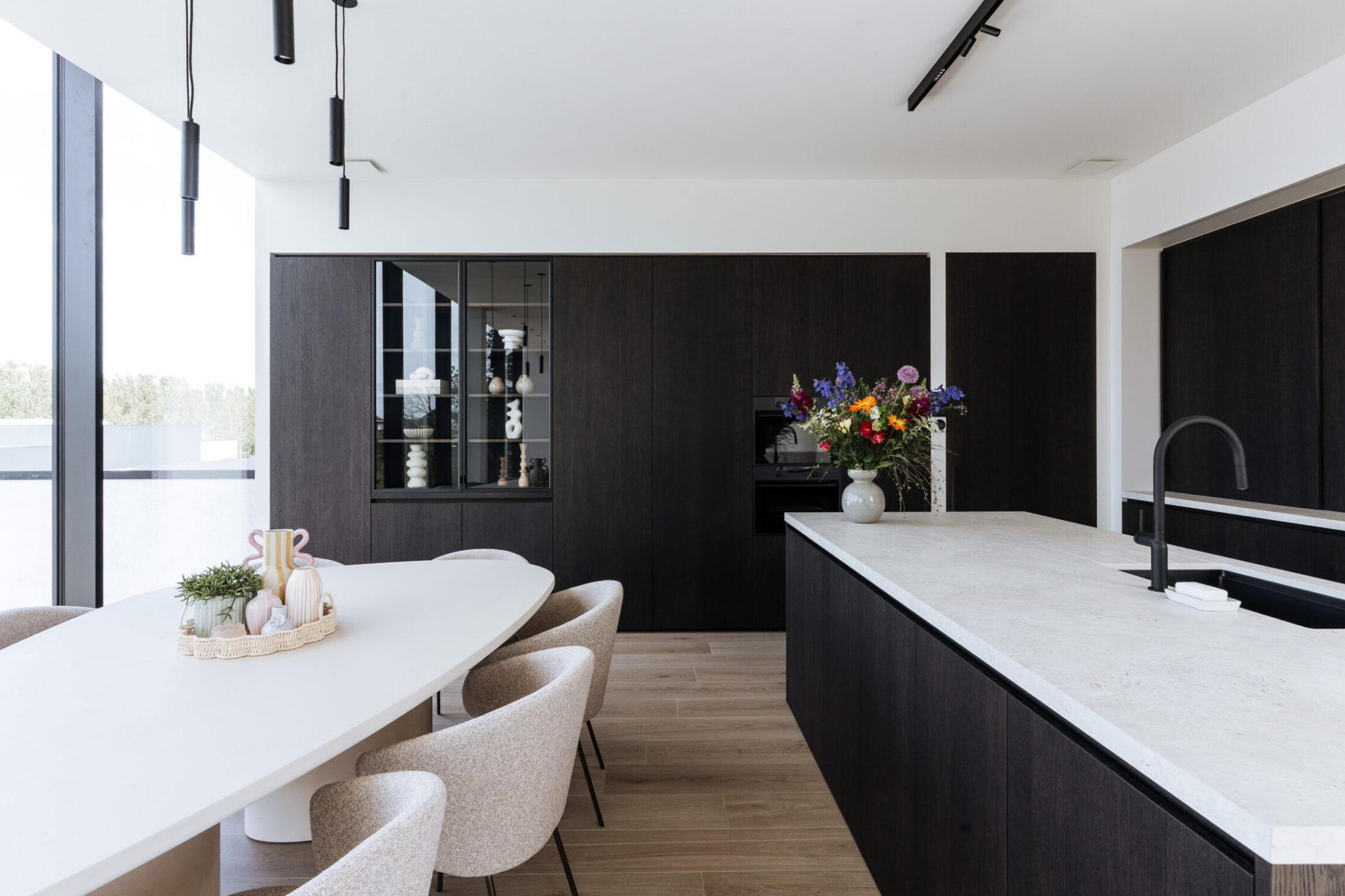 Moderne keuken met donkere houten fronten, wit werkblad op het eiland en vitrinekast in Lendelede, Kaster Keukens