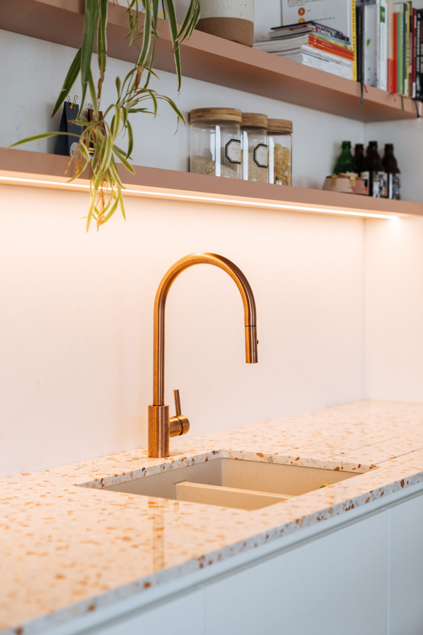 Detail van een moderne keuken met terrazzo werkblad, koperen kraan en verlichte open rekken in Merelbeke, Kaster Keukens