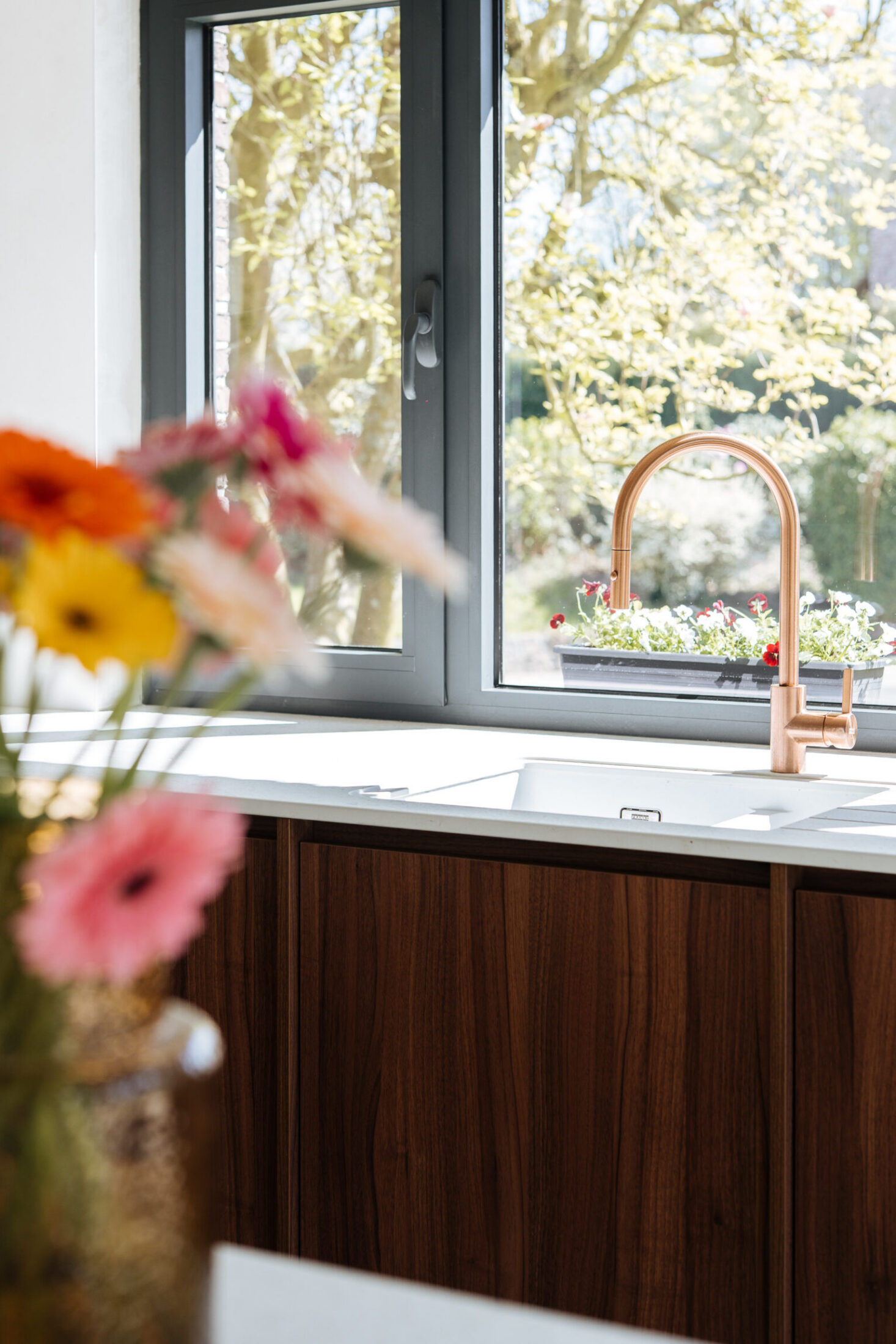 Detail van een moderne keuken met notelaar fronten, wit werkblad en koperen kraan aan het raam in Oosterzele, Kaster Keukens