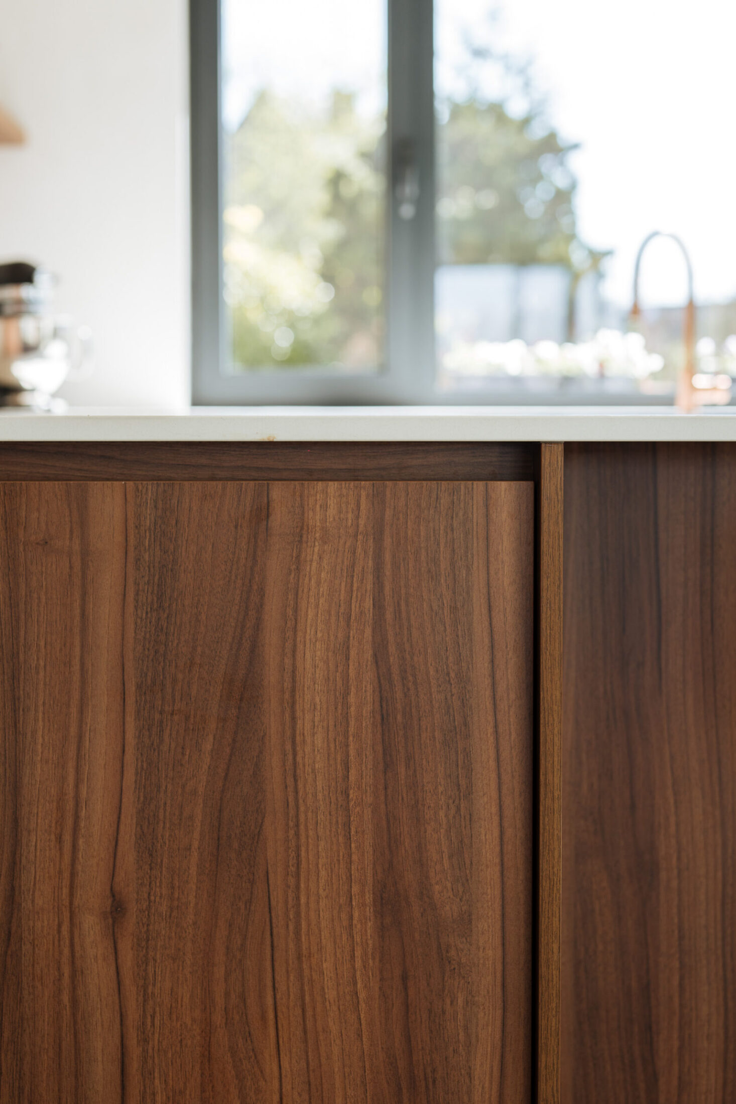 Detail van een moderne keuken met grepenloze notelaar fronten en wit werkblad in Oosterzele, Kaster Keukens