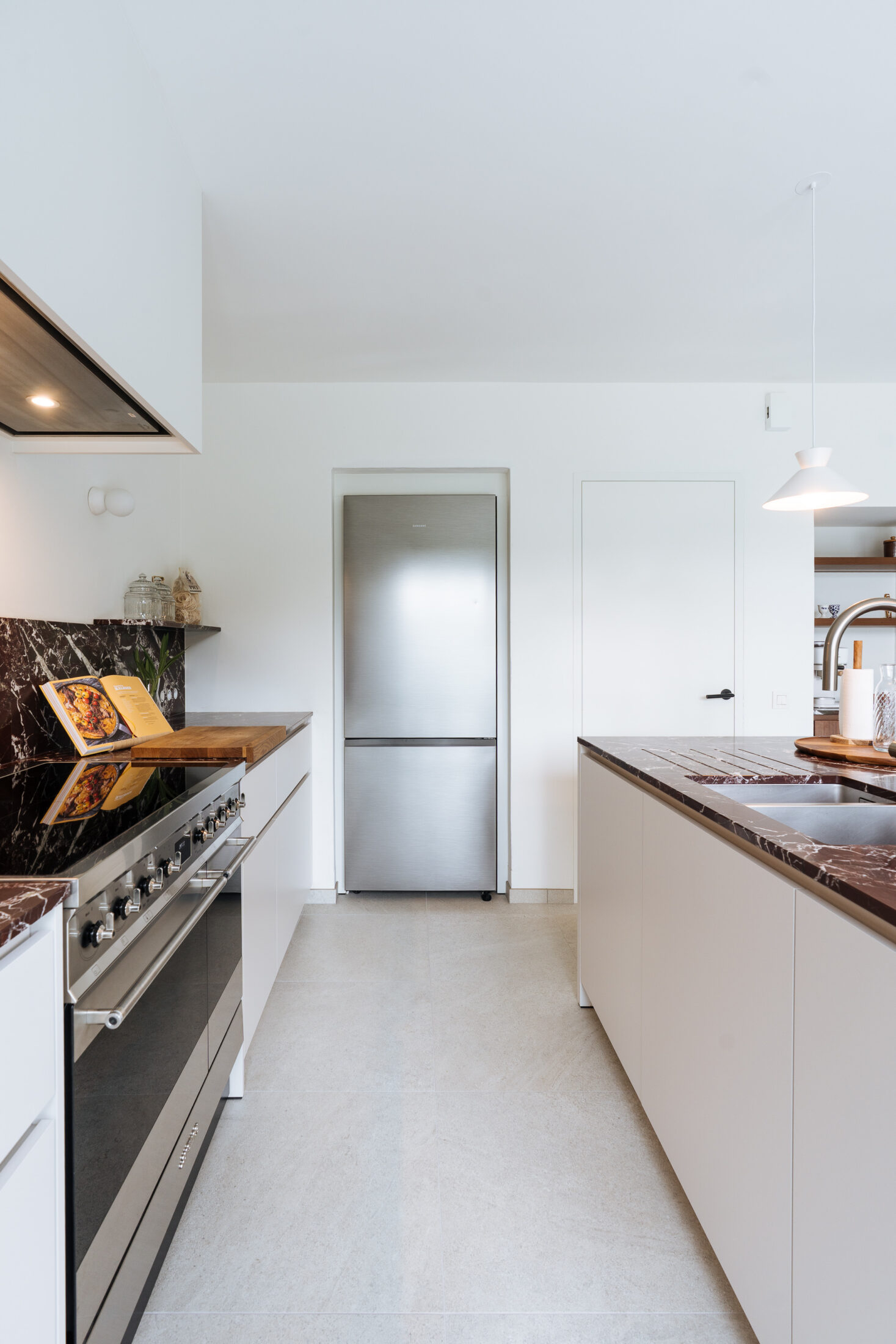 Moderne keuken met witte fronten, inox fornuis en bordeaux marmeren werkblad in Waregem, Kaster Keukens