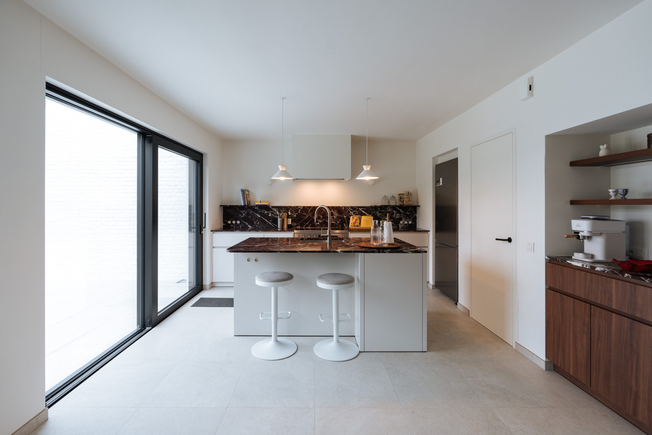 Moderne keuken met wit kookeiland, witte barkrukken en groot schuifraam in Waregem, Kaster Keukens