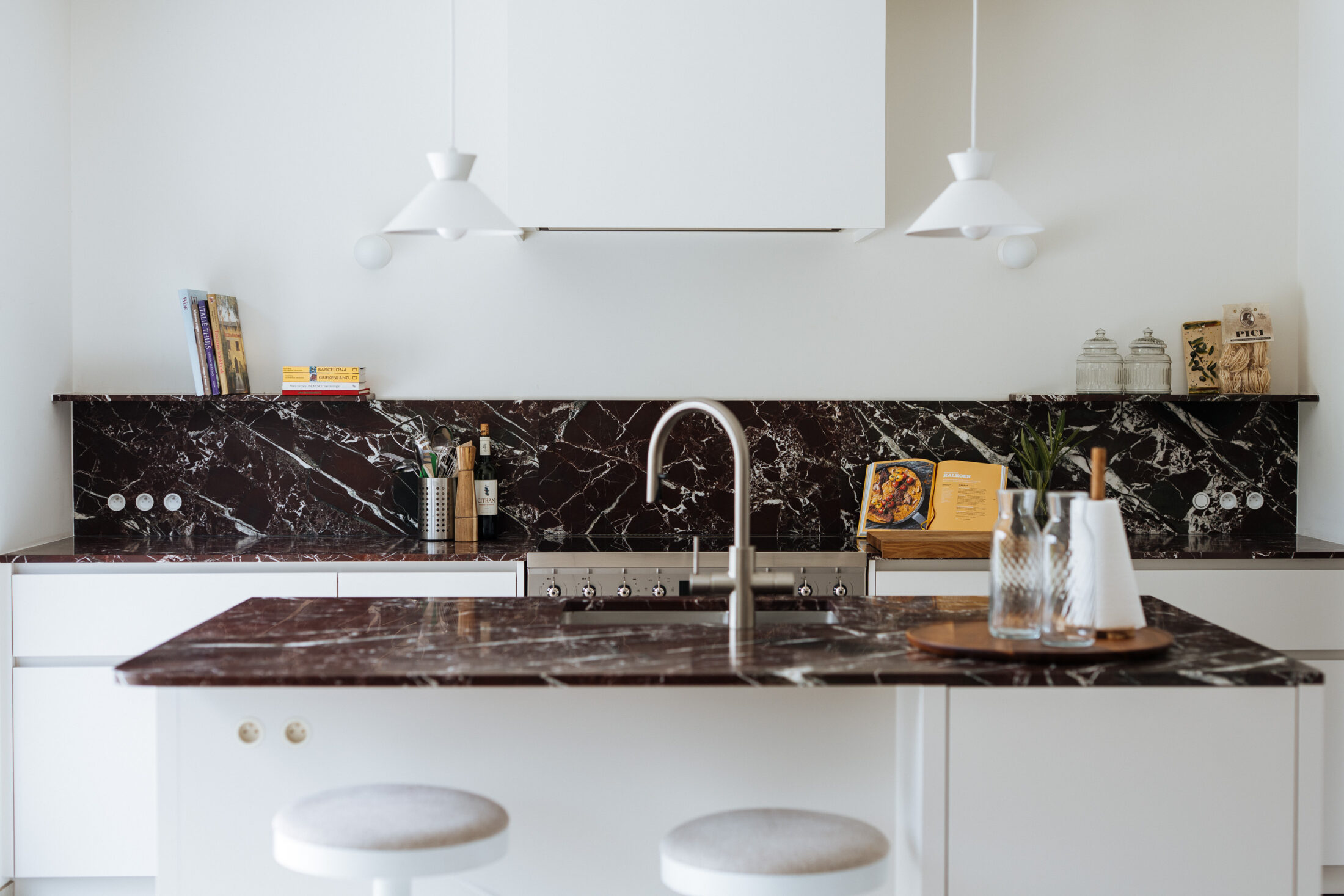 Moderne keuken met witte fronten, bordeaux marmeren werkblad en spatwand en witte hanglampen in Waregem, Kaster Keukens