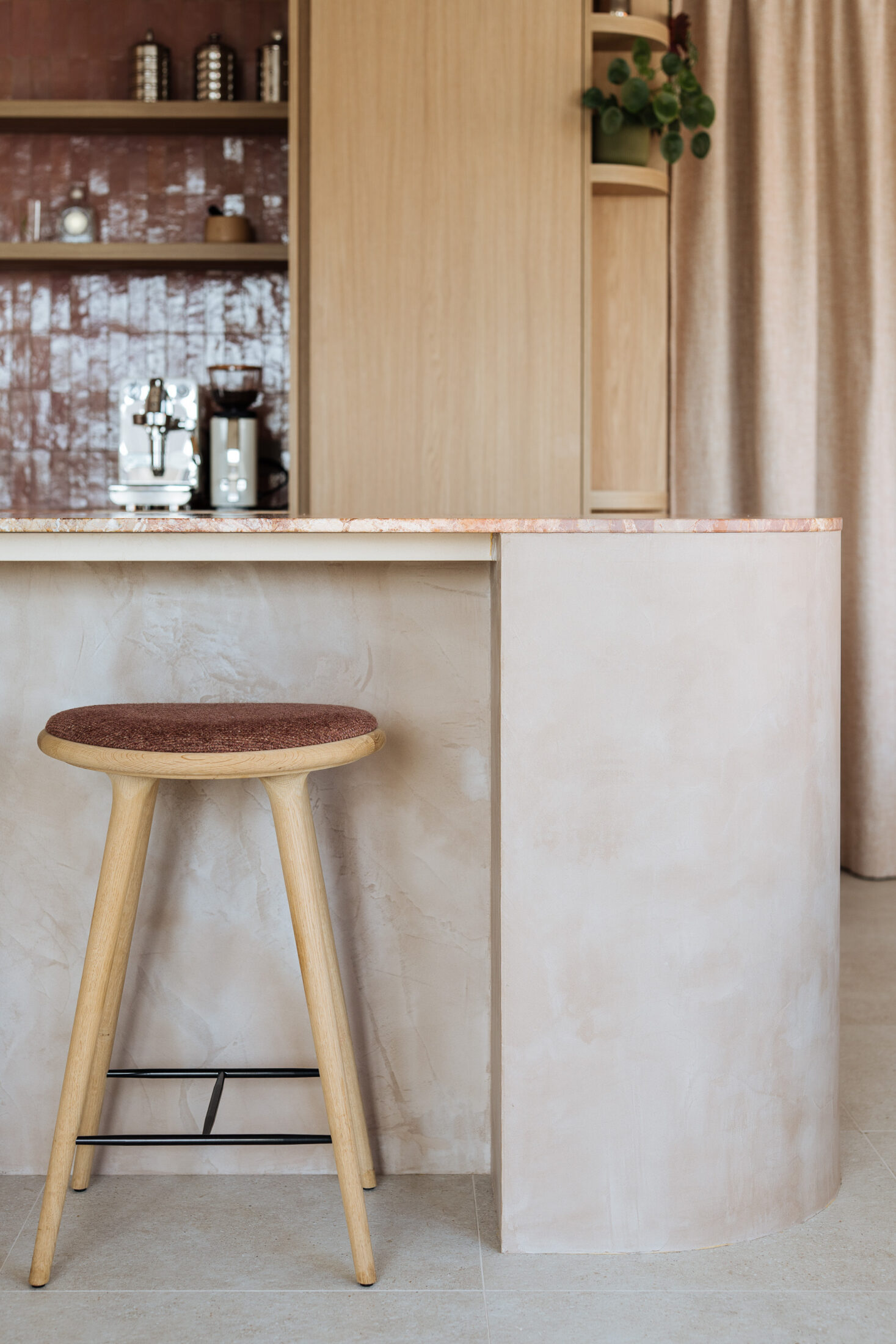 Detail van een japandi keuken met houten barkruk aan een licht eiland en roze wandtegels in Oostende, Kaster Keukens