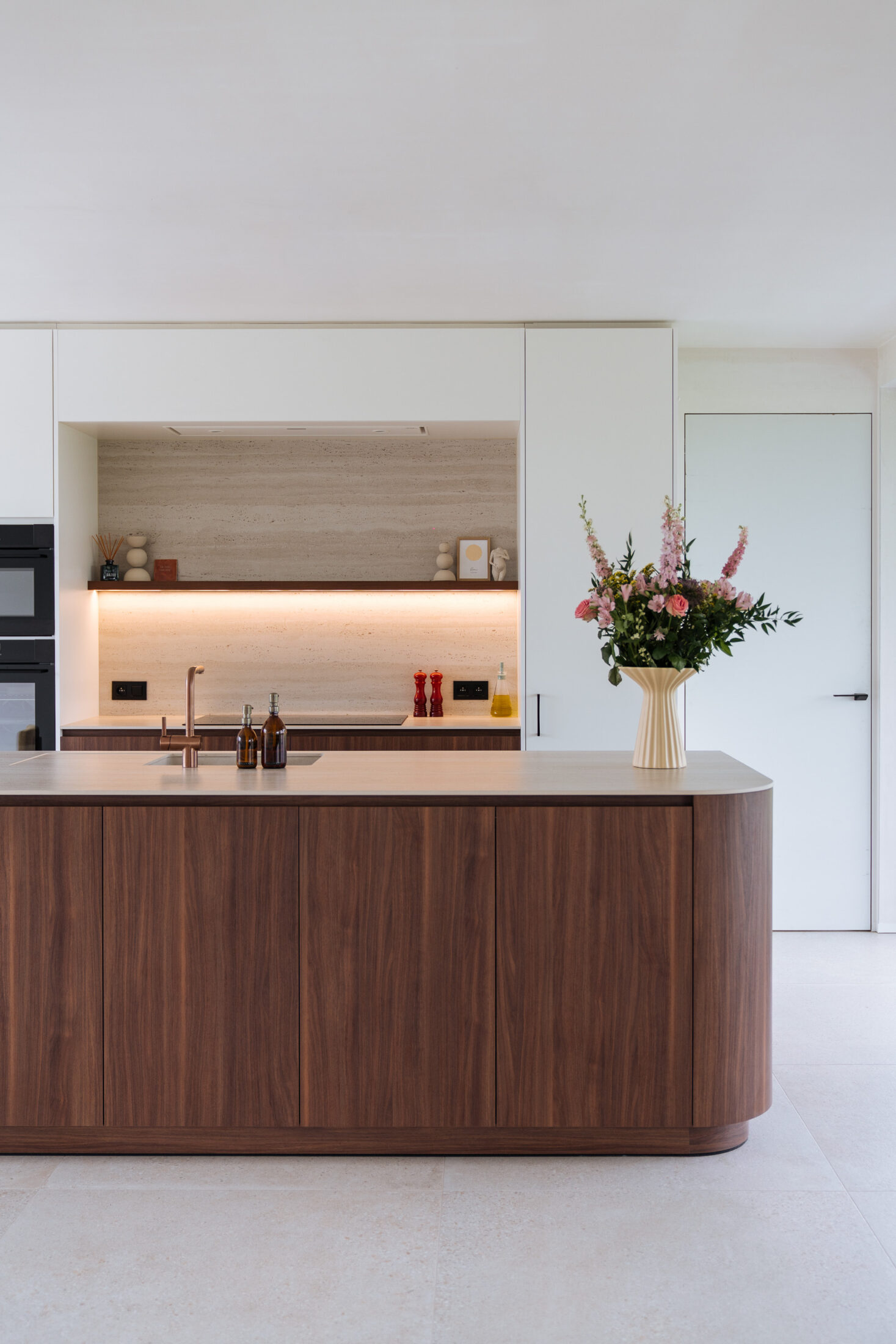 Moderne keuken met afgerond eiland in notelaar, witte kastenwand en verlichte nis in Hooglede, Kaster Keukens
