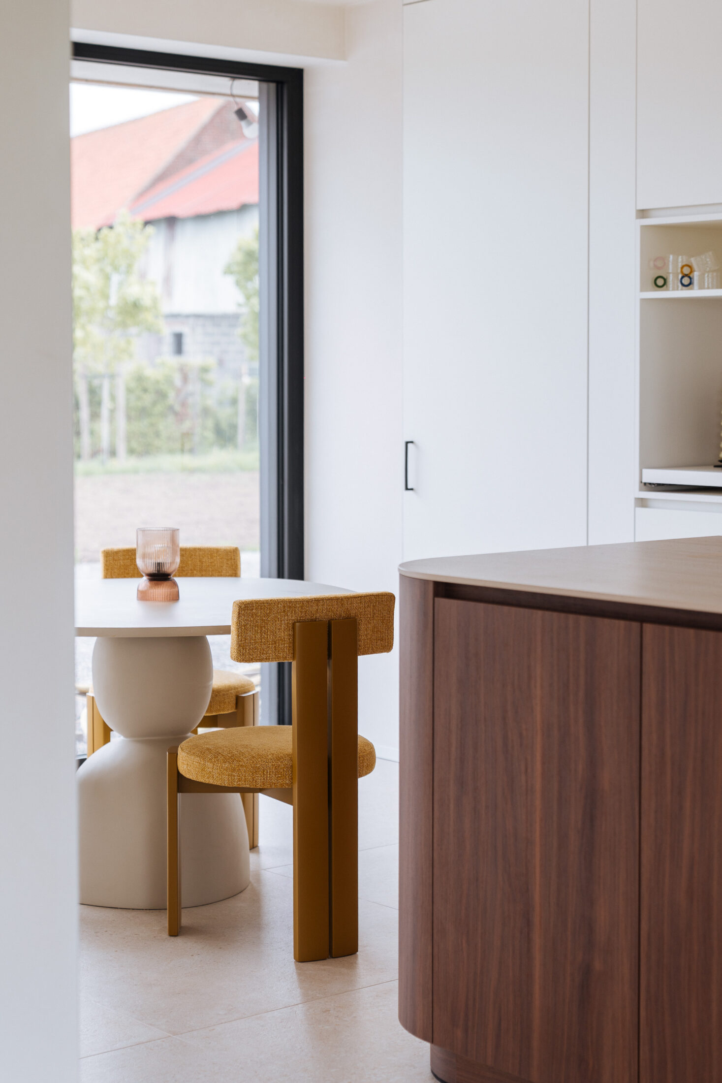 Detail van een moderne keuken met notelaar eiland en gele stoelen aan de eettafel in Hooglede, Kaster Keukens