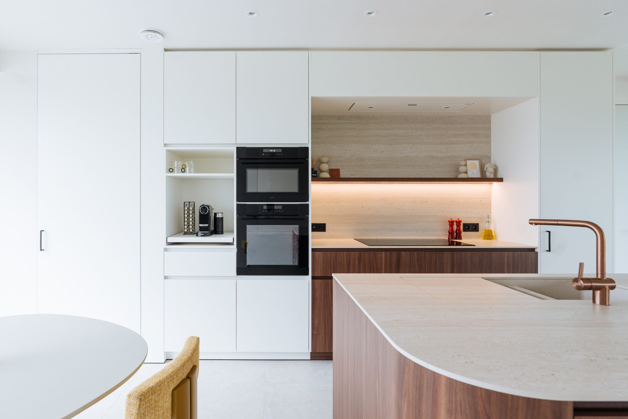 Moderne keuken met witte kastenwand, twee inbouwovens en afgerond eiland met koperen kraan in Hooglede, Kaster Keukens