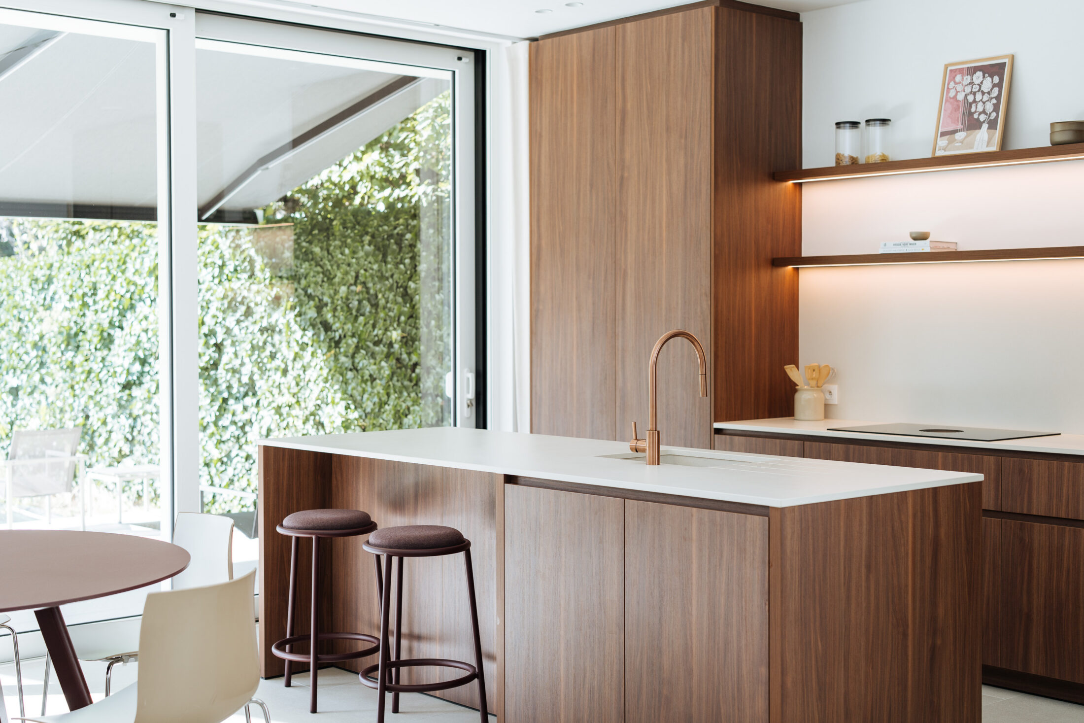 Moderne keuken met notelaar fronten, wit werkblad, koperen kraan en bordeaux barkrukken in Kortrijk, Kaster Keukens