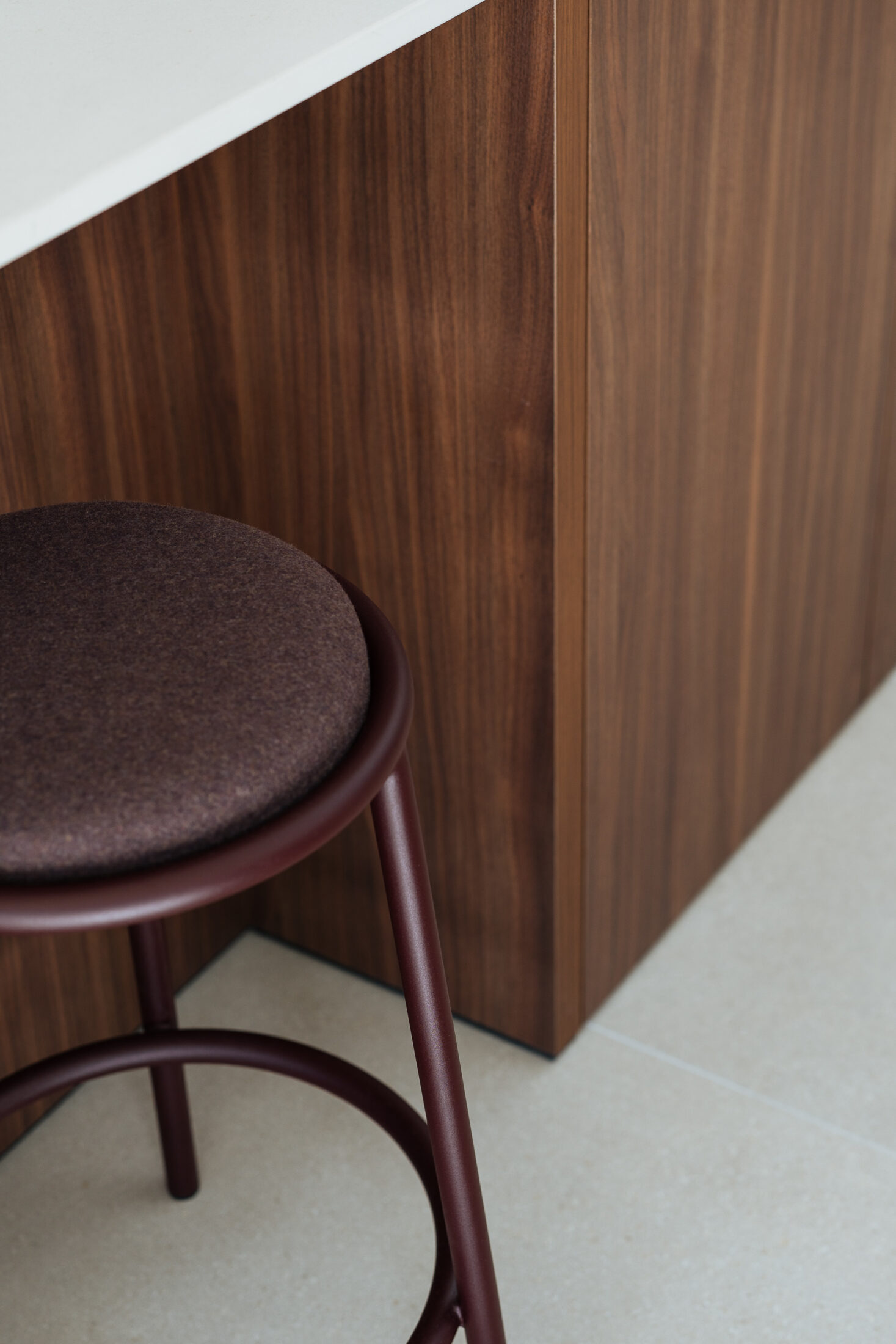 Detail van een moderne keuken met bordeaux barkruk aan een notelaar eiland in Kortrijk, Kaster Keukens