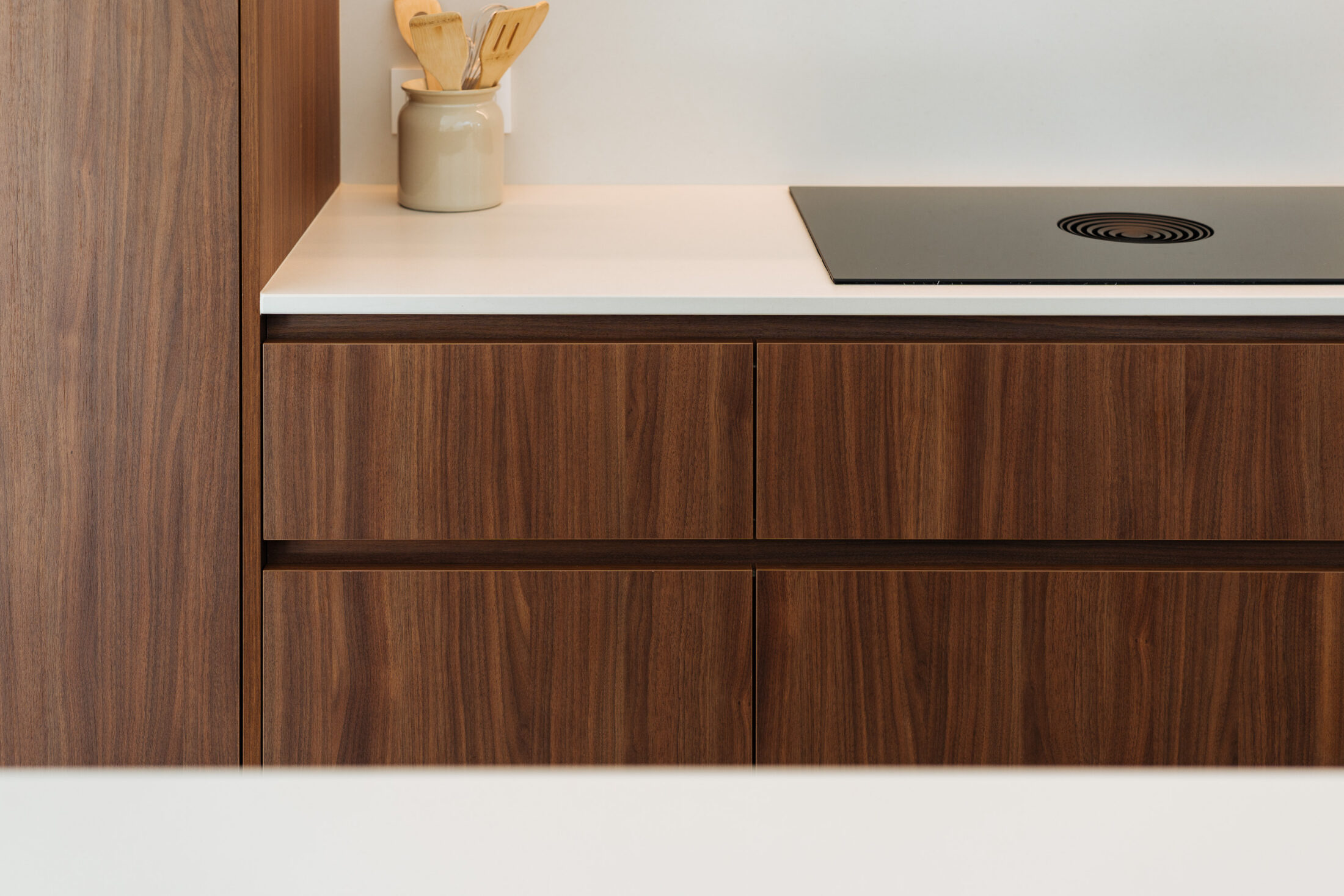 Detail van een moderne keuken met grepenloze notelaar laden, wit werkblad en kookplaat in Kortrijk, Kaster Keukens