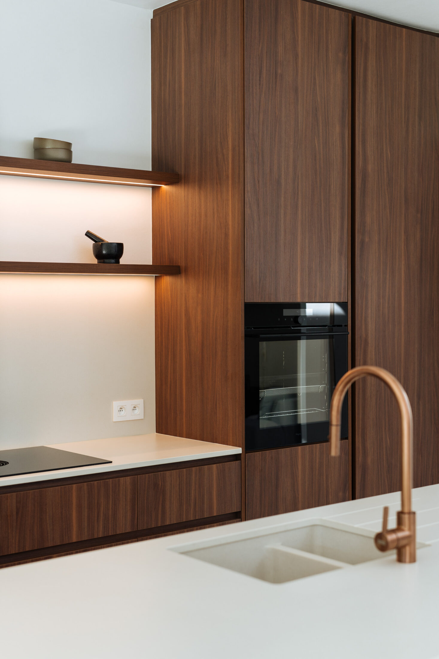 Detail van een moderne keuken met koperen kraan, spoelbak en notelaar hoge kasten in Kortrijk, Kaster Keukens