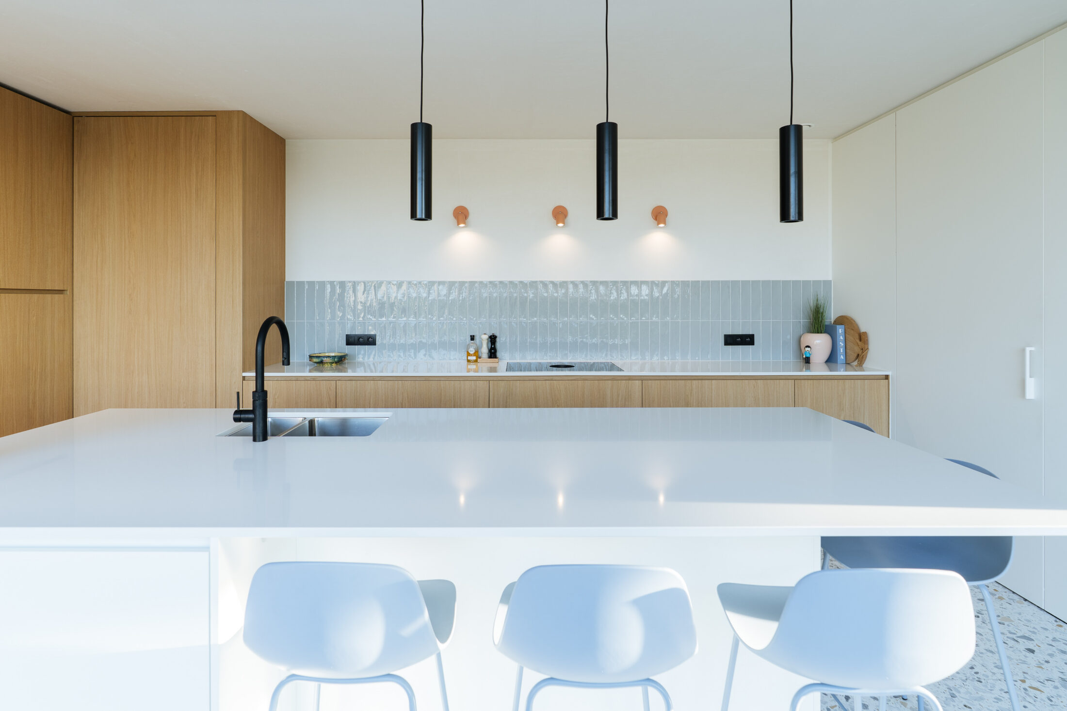 Moderne keuken met eiken fronten, wit kookeiland, lichtblauwe barkrukken en zwarte hanglampen in Torhout, Kaster Keukens