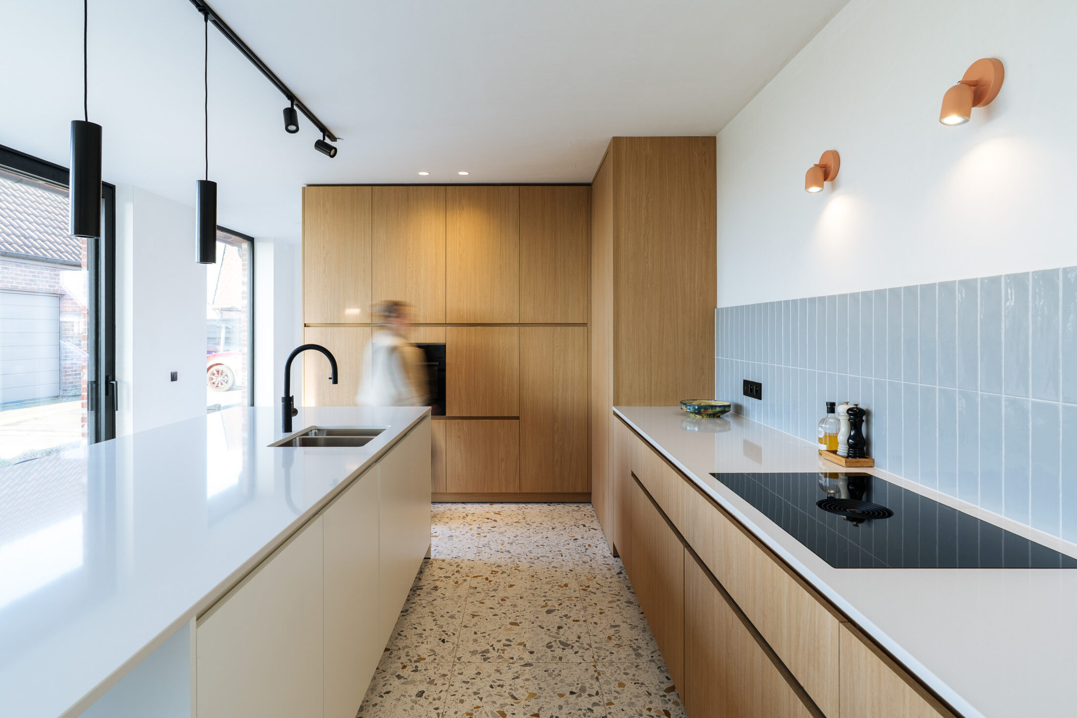 Moderne keuken met eiken kastenwand, wit werkblad, lichtblauwe wandtegels en terrazzovloer in Torhout, Kaster Keukens