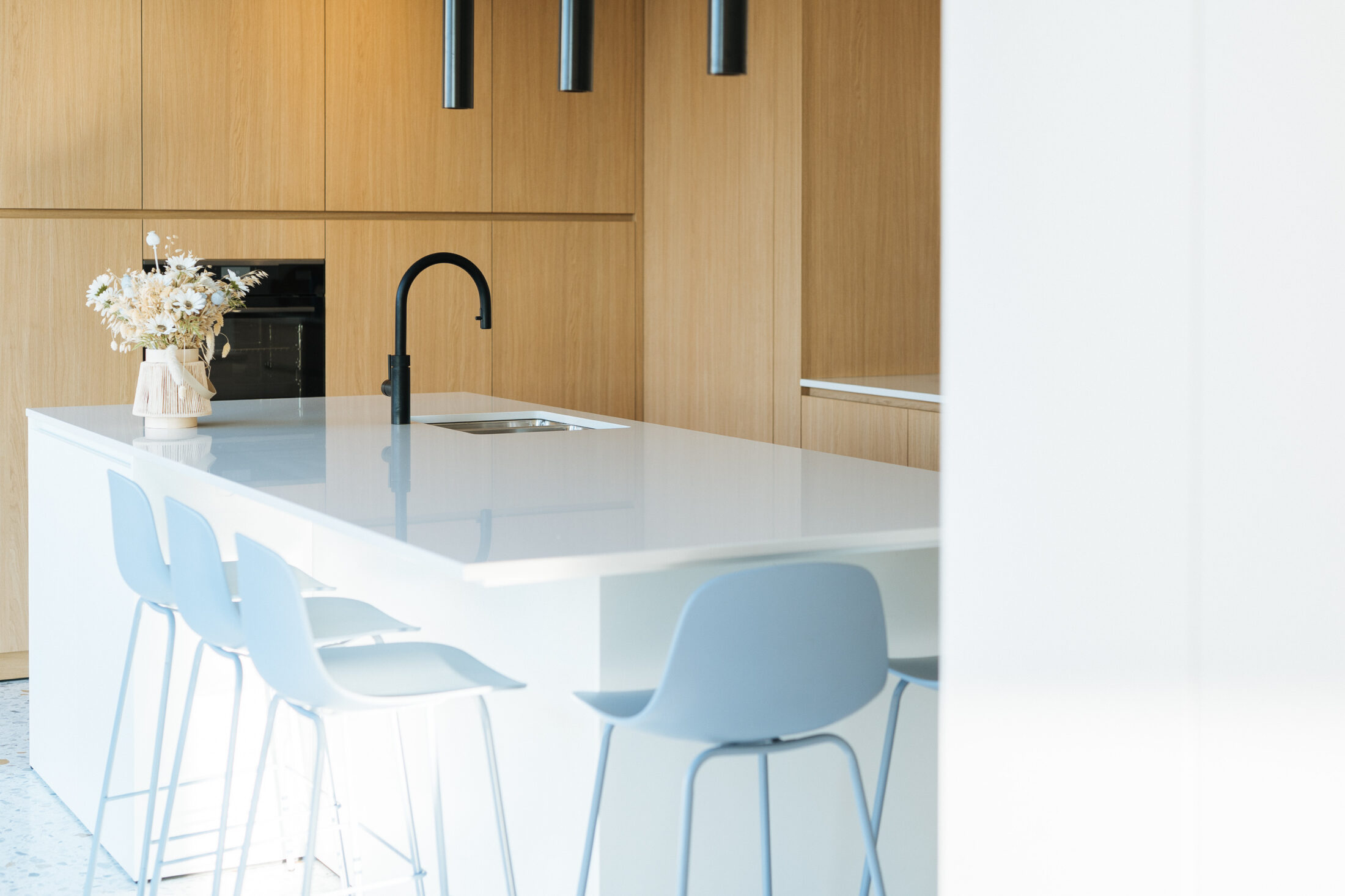 Moderne keuken met wit kookeiland, zwarte kraan en ingebouwde oven in een eiken kastenwand in Torhout, Kaster Keukens