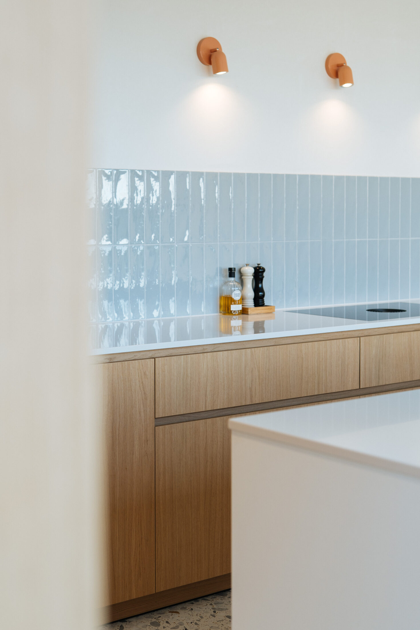 Detail van een moderne keuken met lichtblauwe wandtegels, eiken onderkasten en koperen wandlampjes in Torhout, Kaster Keukens