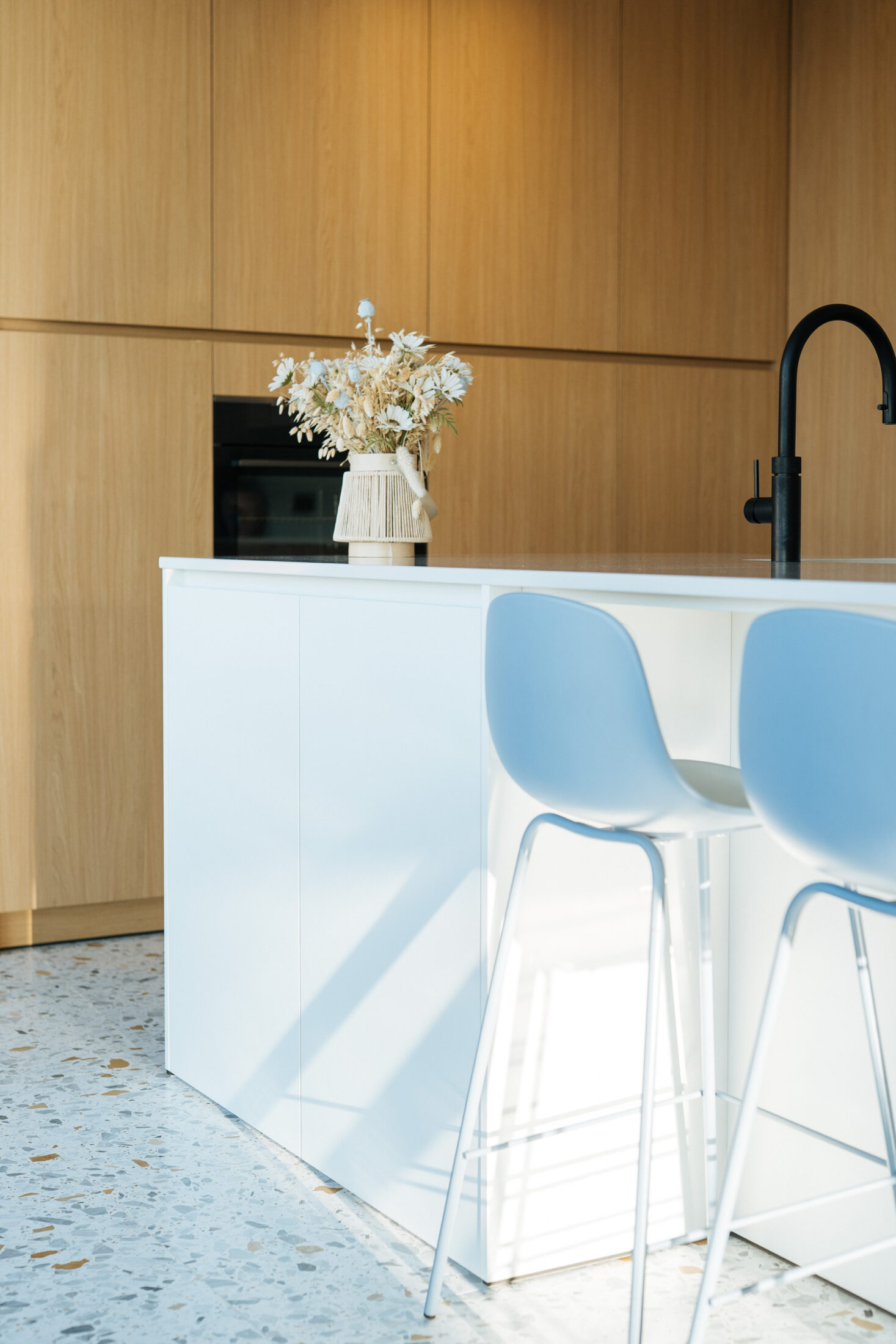 Detail van een moderne keuken met wit eiland en lichtblauwe barkrukken voor eiken hoge kasten in Torhout, Kaster Keukens