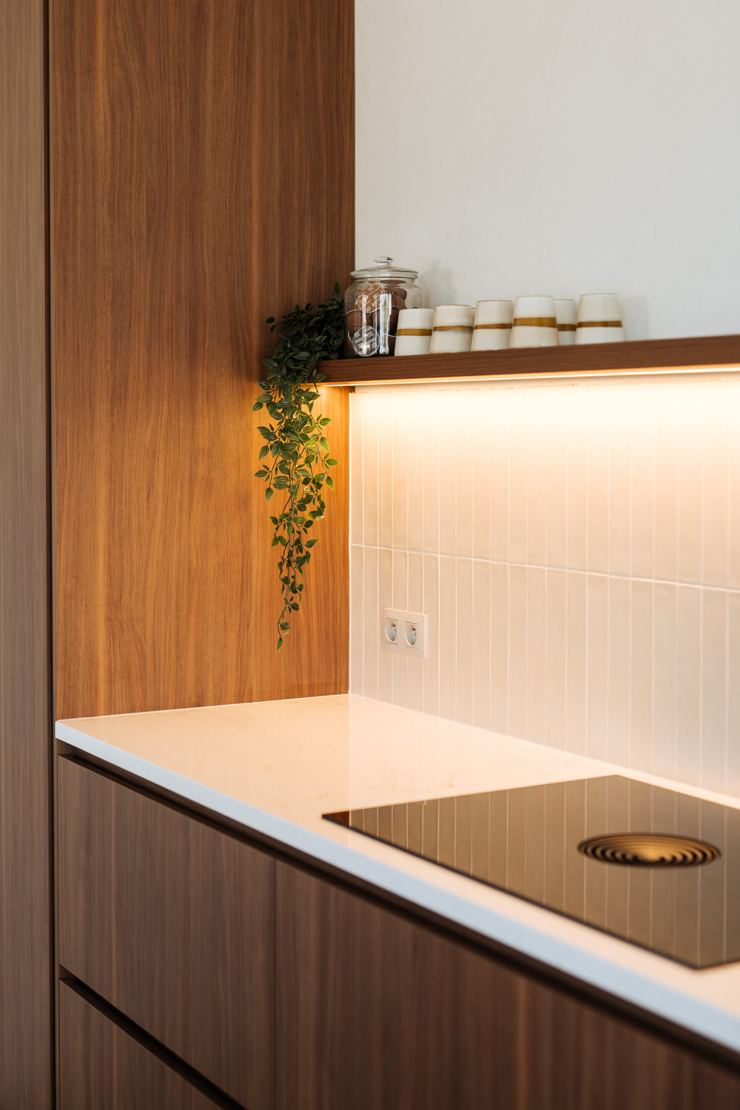 Moderne keuken met notelaarlook fronten, wit composiet werkblad, koperkleurige kraan en lichte barkrukken met houten onderstel, Kaster Keukens.