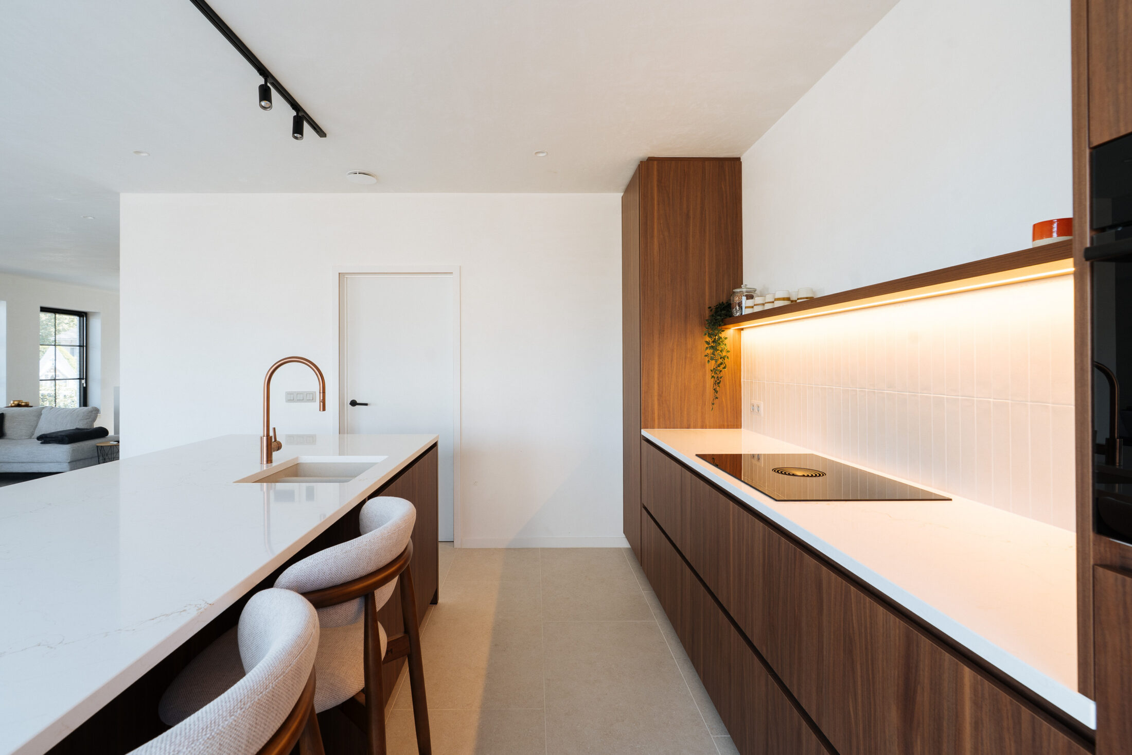 Moderne keuken met notelaarlook fronten, wit composiet werkblad, koperkleurige kraan en lichte barkrukken met houten onderstel, Kaster Keukens.