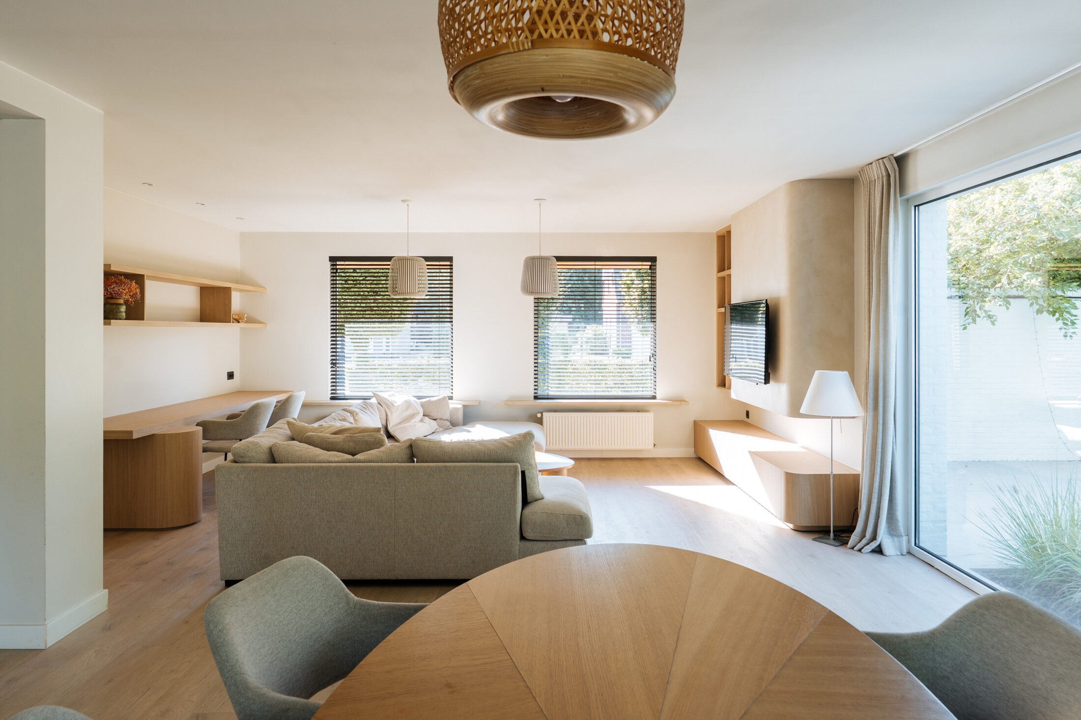 Tv-meubel op maat in lichte eikenlook met afgeronde hoek en open vakkenkast naast een beige tv-wand, Kaster Keukens.