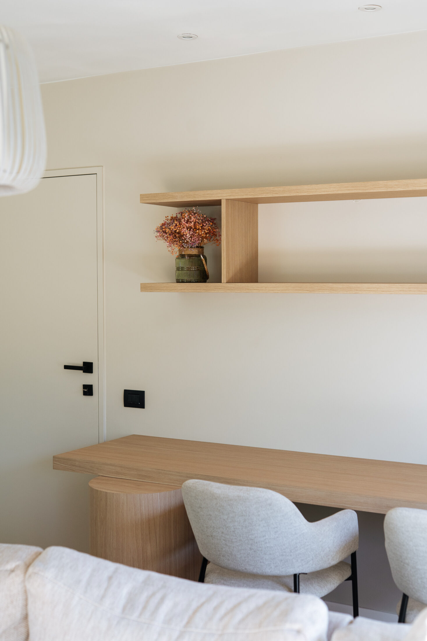 Tv-meubel op maat in lichte eikenlook met afgeronde hoek en open vakkenkast naast een beige tv-wand, Kaster Keukens.