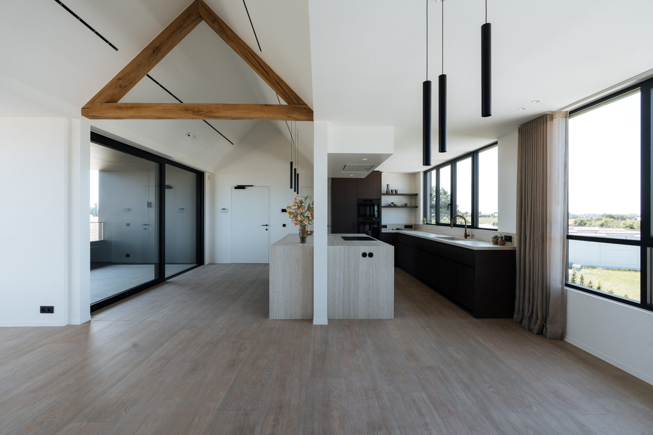 Moderne keuken met donkere houtlook fronten, licht werkblad met doorlopende zijwanden, ruim kookeiland en zwarte hanglampen, Kaster Keukens.