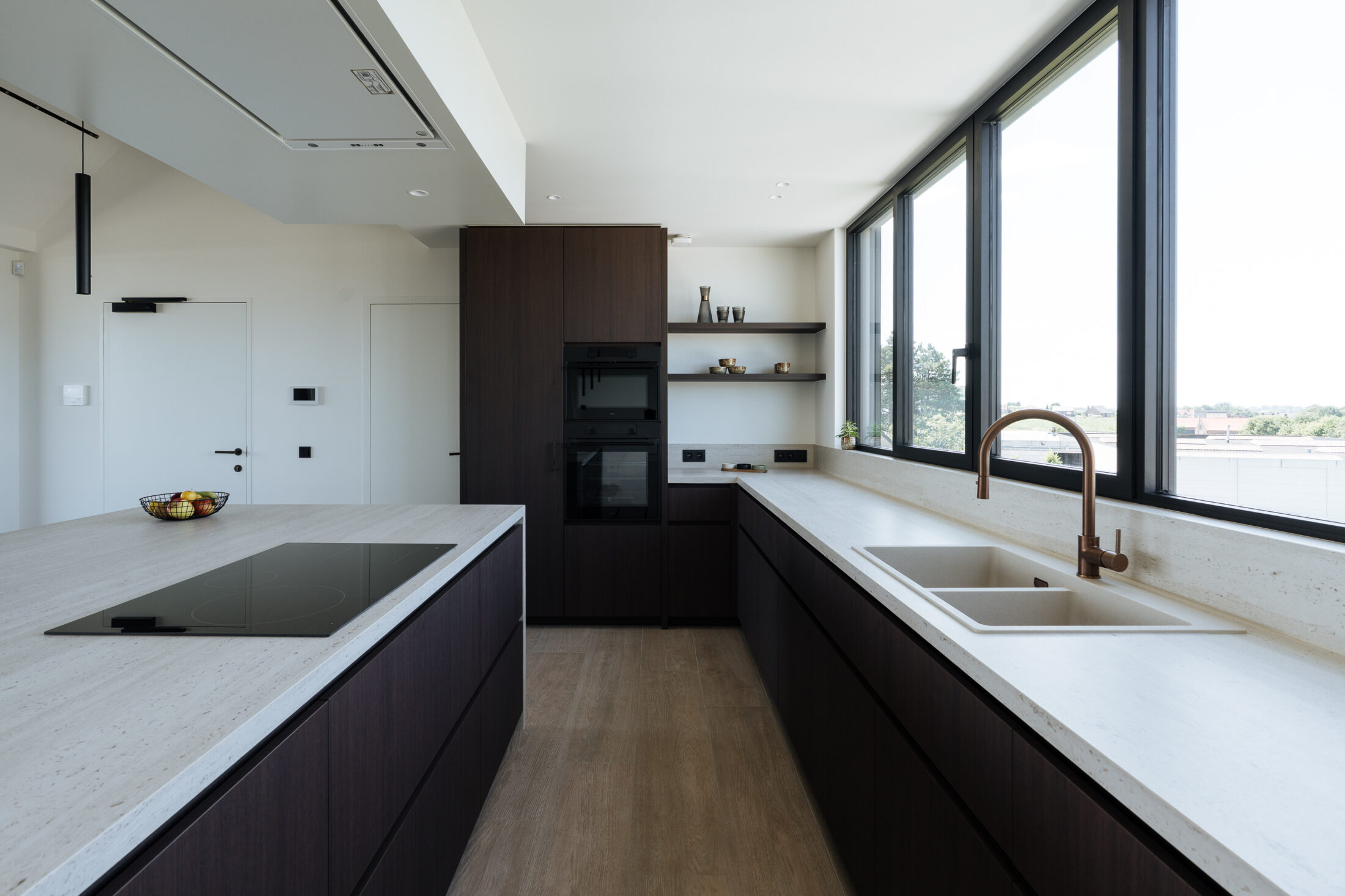 Moderne keuken met donkere houtlook fronten, licht werkblad met doorlopende zijwanden, ruim kookeiland en zwarte hanglampen, Kaster Keukens.