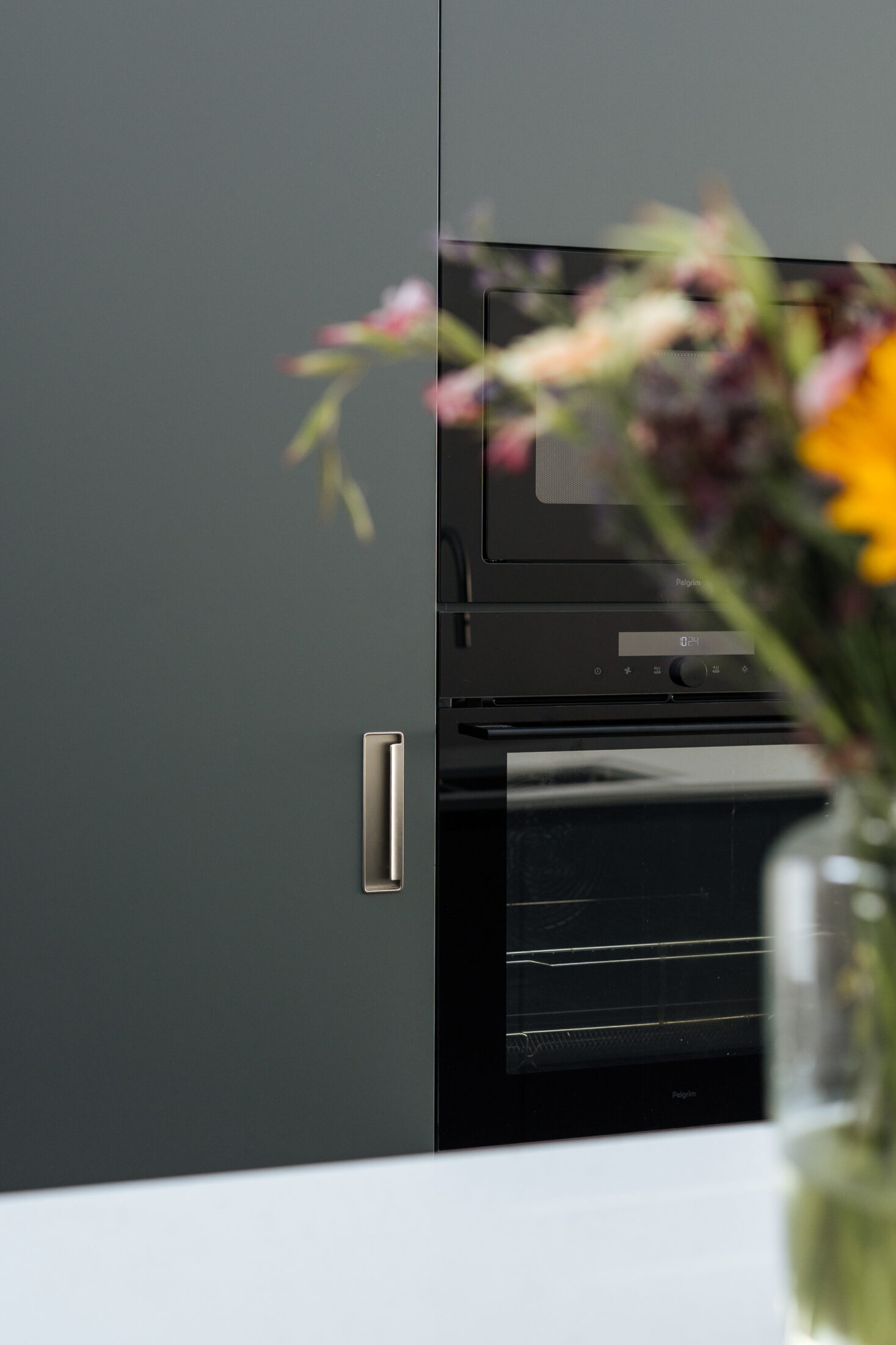 Moderne keuken met donkergroene fronten, wit werkblad, lang kookeiland met zitplaatsen en een open koffienis, Kaster Keukens.