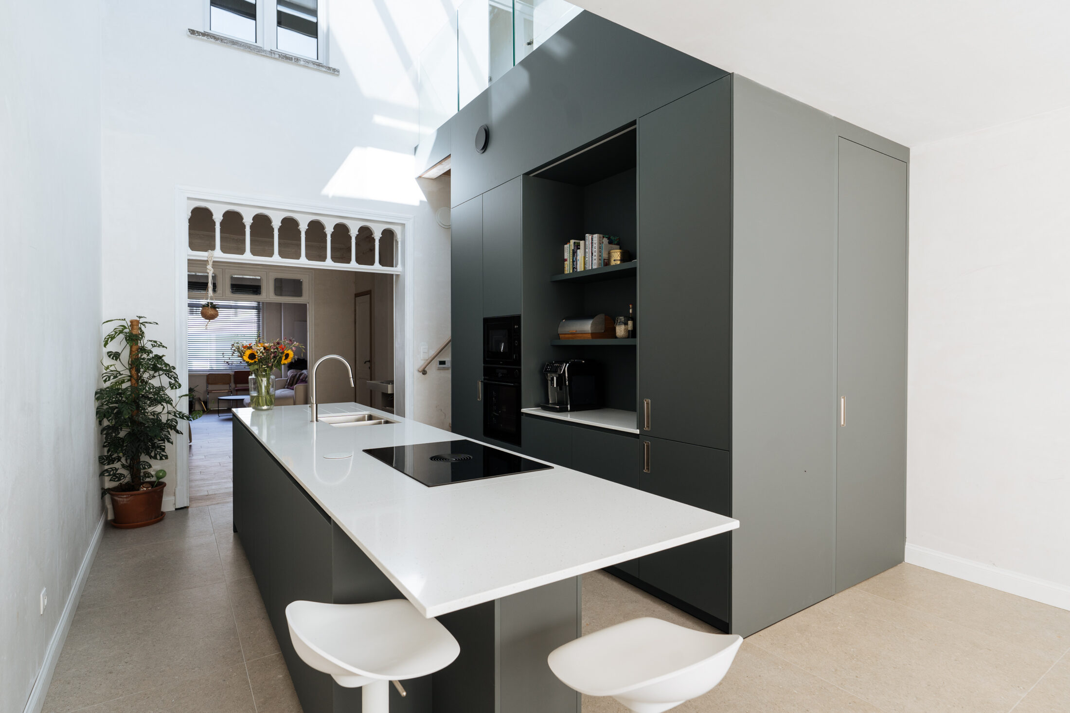Moderne keuken met donkergroene fronten, wit werkblad, lang kookeiland met zitplaatsen en een open koffienis, Kaster Keukens.