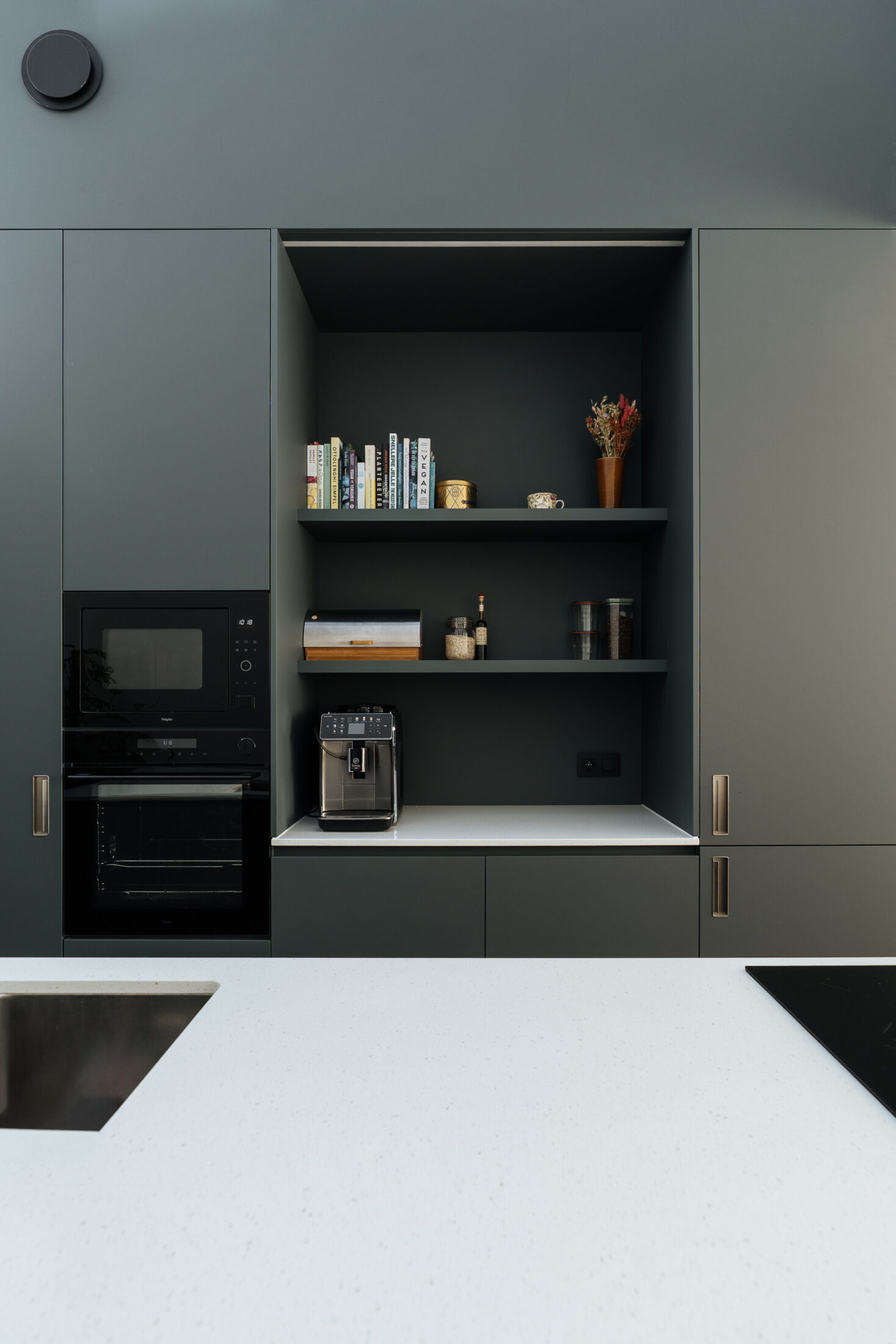 Moderne keuken met donkergroene fronten, wit werkblad, lang kookeiland met zitplaatsen en een open koffienis, Kaster Keukens.