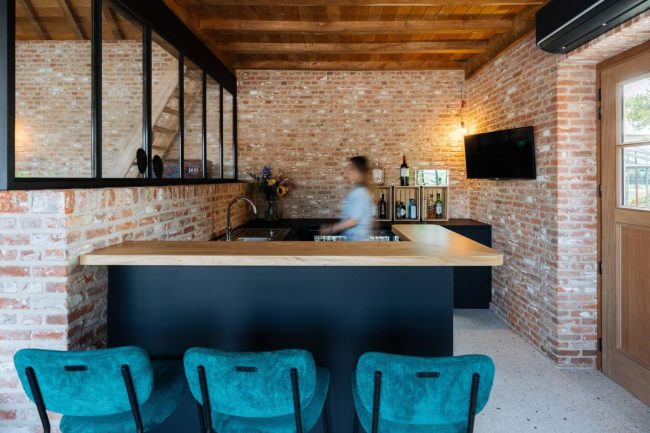 Bar op maat met zwarte fronten, houten toog en blauwe barkrukken tegen een bakstenen muur in Beveren, Kaster Keukens