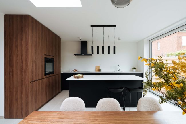 Moderne keuken met notelaar kastenwand, zwart kookeiland en zwarte hanglampen, Kaster Keukens