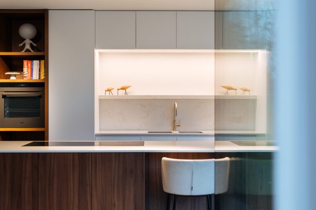 Moderne keuken met notelaar eiland, lichtgrijze kasten en verlichte nis met koperkleurige kraan in Drongen, Kaster Keukens