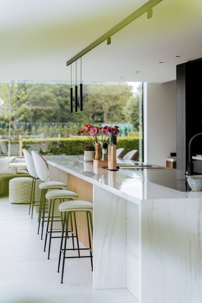 Moderne keuken met wit kookeiland, groene barkrukken en grote ramen in Gent, Kaster Keukens