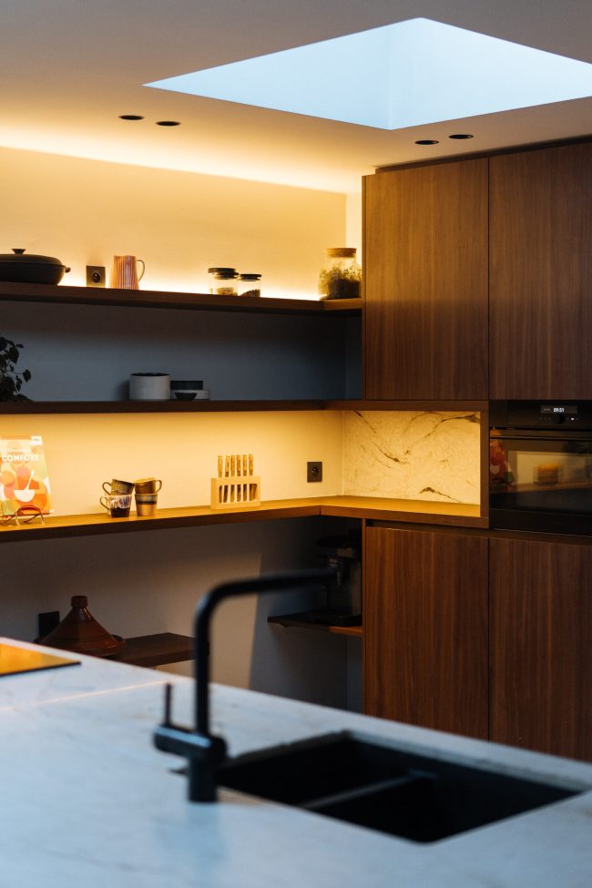 Moderne keuken met notelaar kasten, verlichte open rekken en marmerlook werkblad in Hooglede, Kaster Keukens