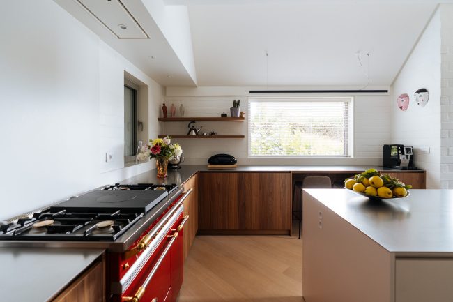 Moderne keuken met rood fornuis, notelaar fronten, wit eiland en open wandplanken in Izegem, Kaster Keukens
