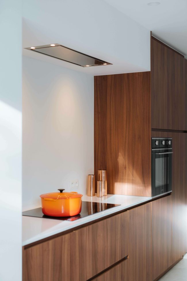 Moderne keuken met notelaar fronten, wit werkblad en plafonddampkap in Kortrijk, Kaster Keukens