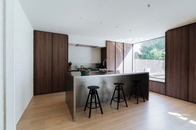 Moderne keuken met notelaar kastenwanden, inox kookeiland en zwarte barkrukken in Mollem, Kaster Keukens