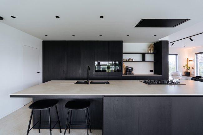 Moderne keuken met zwarte fronten, groot kookeiland met licht werkblad en zwarte barkrukken in Moorsele, Kaster Keukens