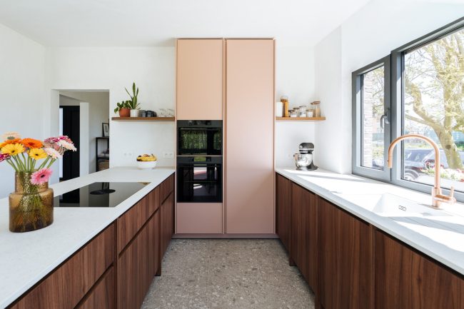 Moderne keuken met roze hoge kasten, notelaar onderkasten, wit werkblad en terrazzovloer in Oosterzele, Kaster Keukens