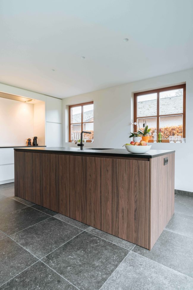 Moderne keuken met notelaar kookeiland, donker werkblad en witte kasten in Passendale, Kaster Keukens