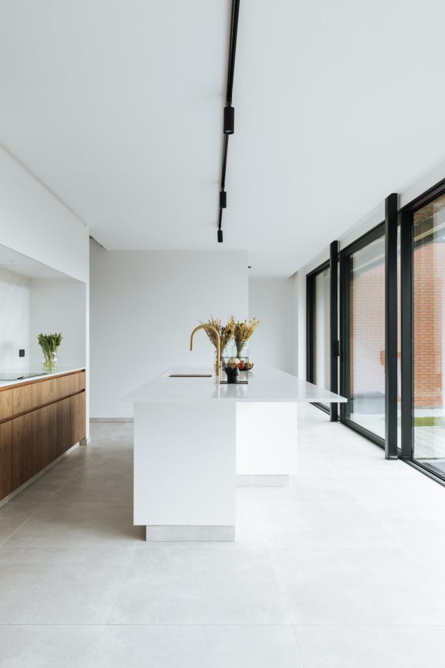 Moderne keuken met wit kookeiland, houten onderkasten en grote ramen in Roeselare, Kaster Keukens
