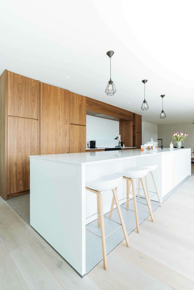 Moderne keuken met houten kastenwand, wit kookeiland en witte barkrukken in Roeselare, Kaster Keukens