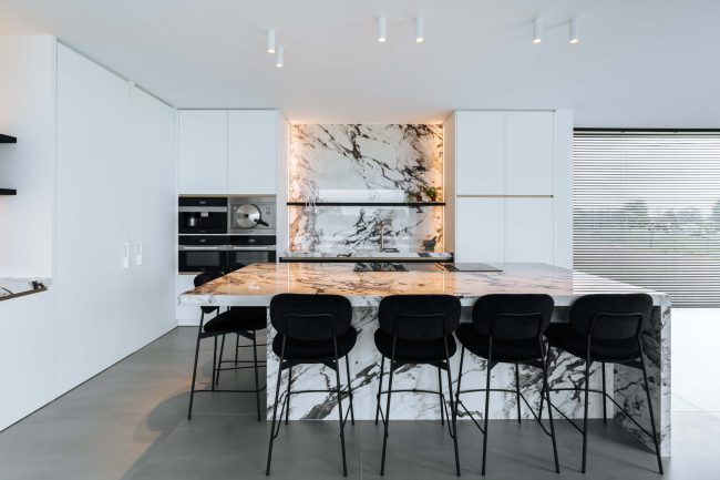 Moderne keuken met marmerlook eiland, zwarte barkrukken en witte kastenwand in Wevelgem, Kaster Keukens