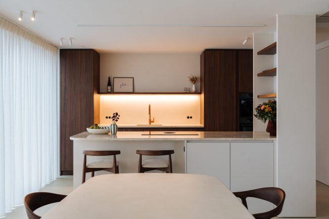 Moderne keuken met notelaar kasten, wit eiland met barkrukken en verlichte nis in Zwevegem, Kaster Keukens
